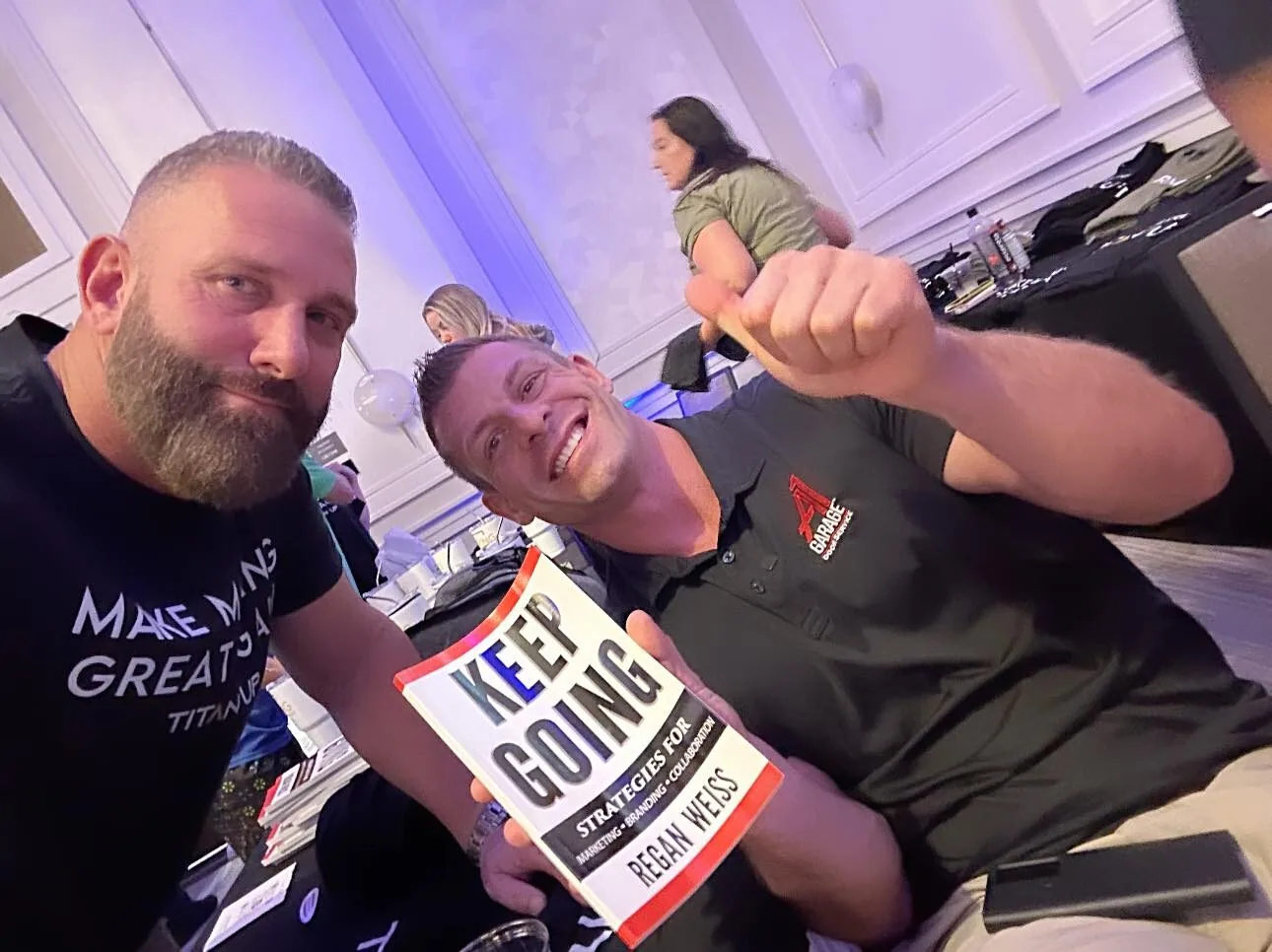 Regan Weiss holding up his book Keep Going with a friend